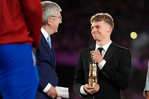 Leon Marchand carries a lantern containing the Olympic flame with IOC President Thomas Bach, left, during the 2024 Summer Olympics closing ceremony